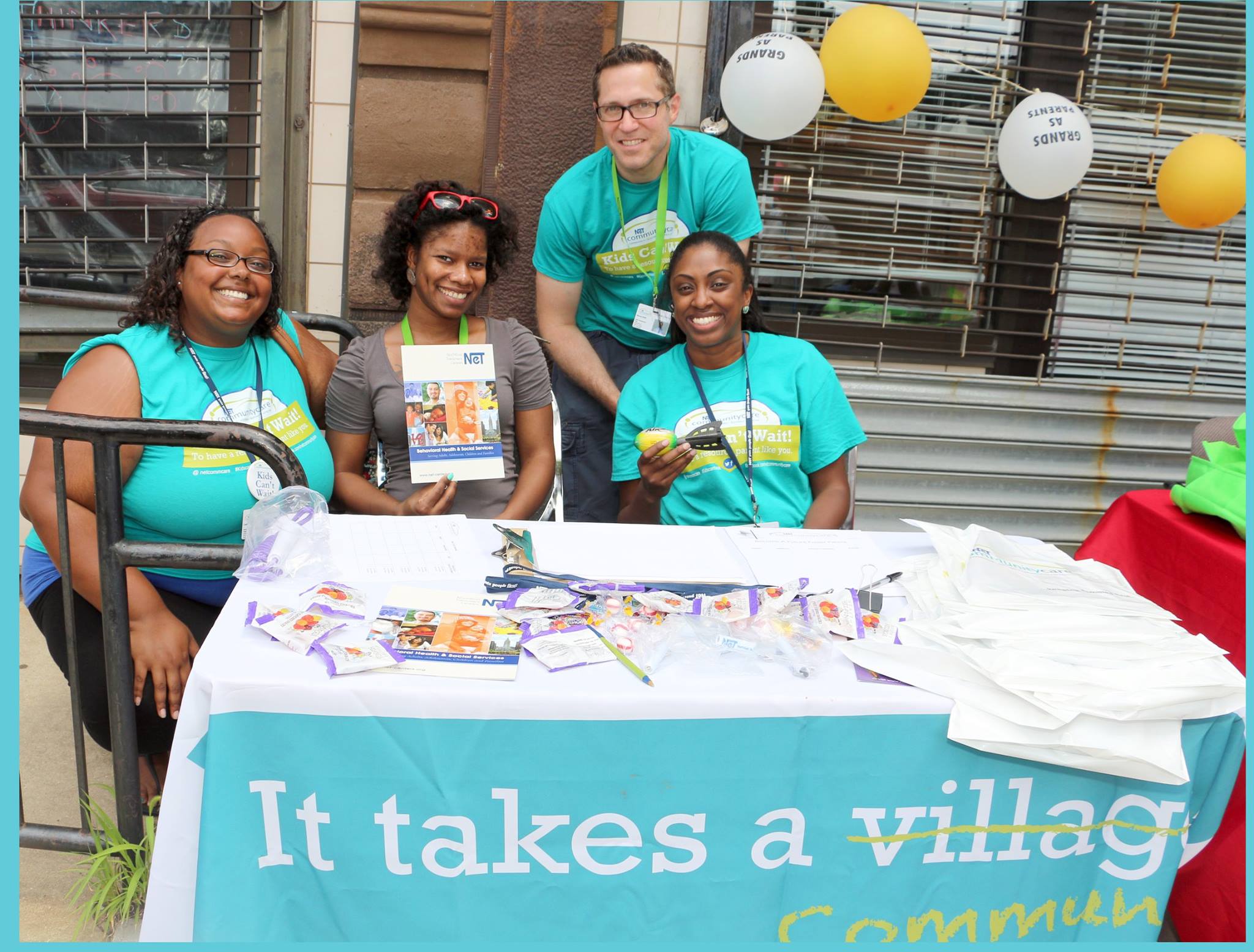 G.A.P's staff at a community outreach table beneath an It Takes A Village banner